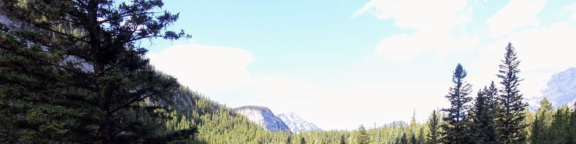 A beautiful view of a par 3 golf hole on a course with mountains in the background, surrounded by forest, on a beautiful sunny day with blue sky, in the rocky mountains near Banff, Alberta