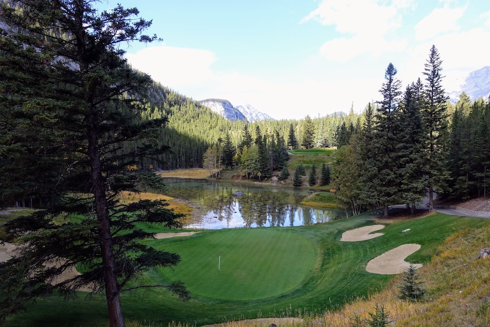 Golfkenttä, jonka yhteydessä on lampi, ja jota ympäröi tiheä metsä ja vuoristo.