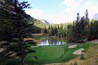 A beautiful view of a par 3 golf hole on a course with mountains in the background, surrounded by forest, on a beautiful sunny day with blue sky, in the rocky mountains near Banff, Alberta