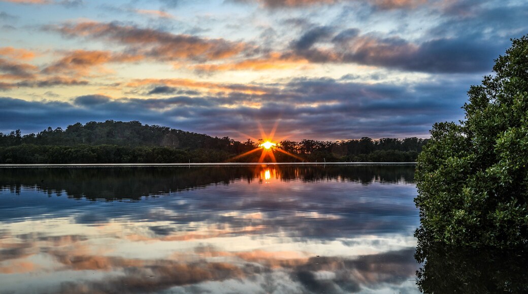 Sun rising against cloudy sky with reflection in river