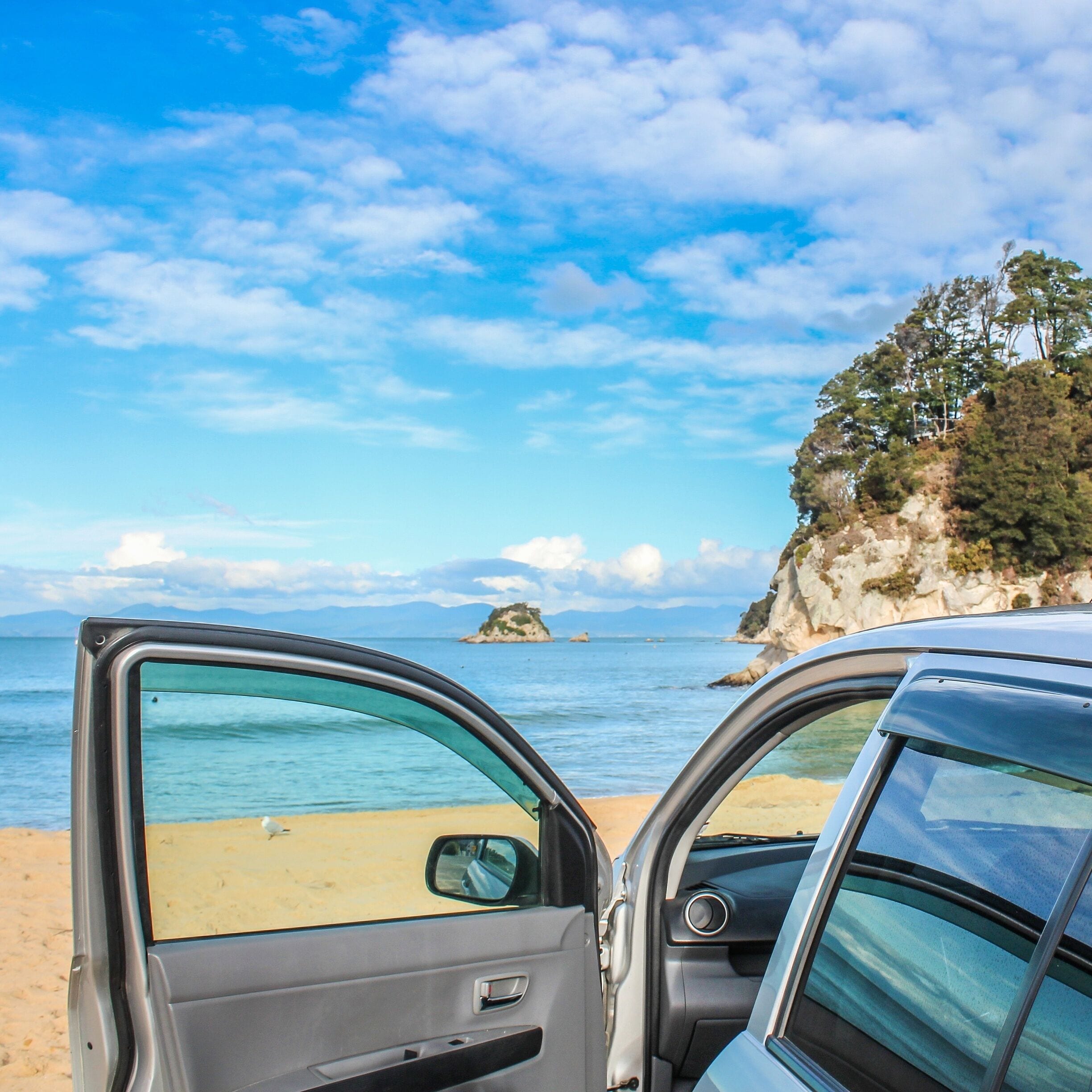 A beach with clear blue water, a sandy shore, and a rocky cliff with trees.