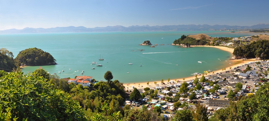 A coastal town with a beach, boats, and a mountainous backdrop.