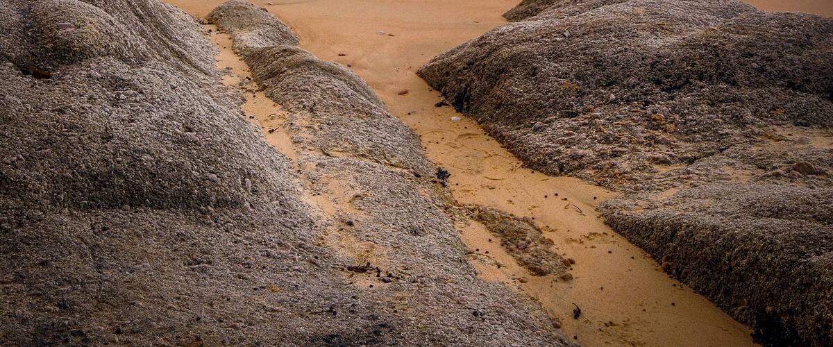 Una playa con rocas grandes al frente y un mar tranquilo.