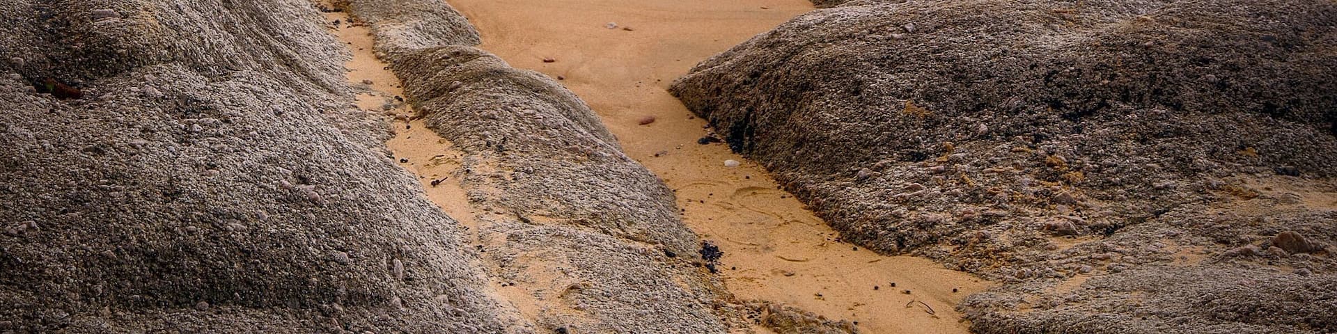 A beach with large rocks in the foreground and a calm sea.