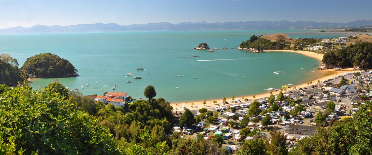 A coastal town with a beach, boats, and a mountainous backdrop.