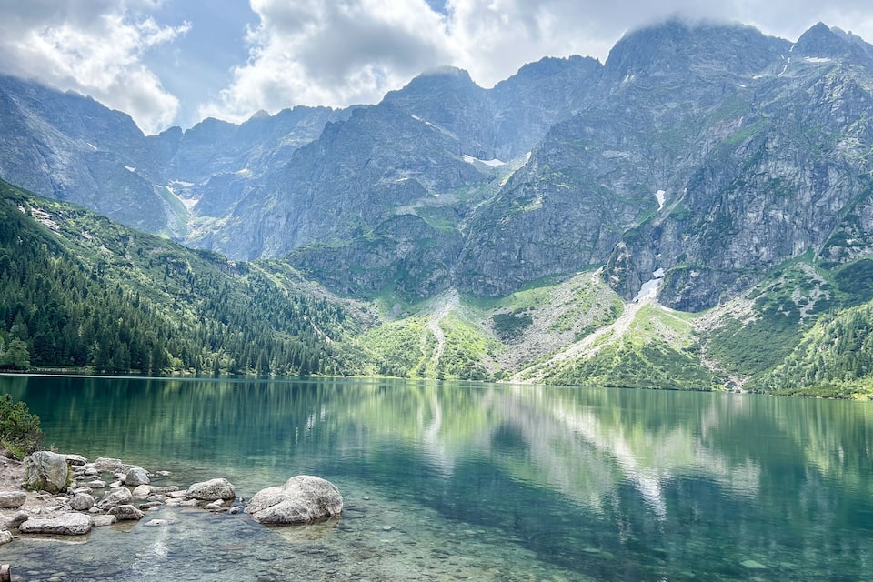 Un lac de montagne aux eaux cristallines, entouré de montagnes escarpées et de forêts denses.