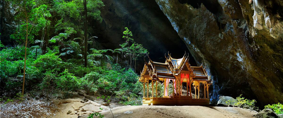 A cave with a traditional Thai temple structure inside, surrounded by dense forest.