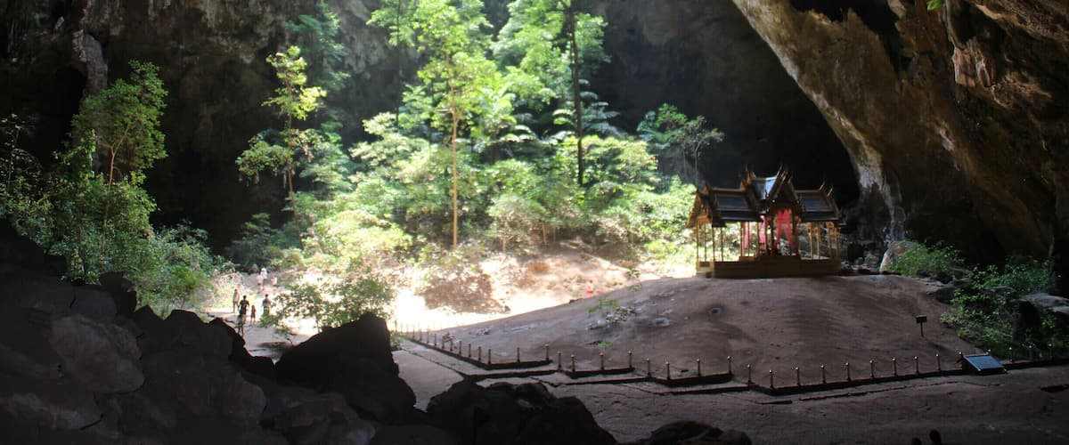 A cave entrance with a temple and lush greenery inside.