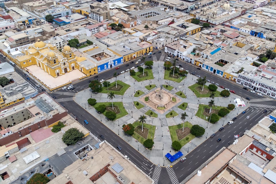 An aerial view of a city square with a prominent yellow cathedral, a central monument, and surrounding buildings.