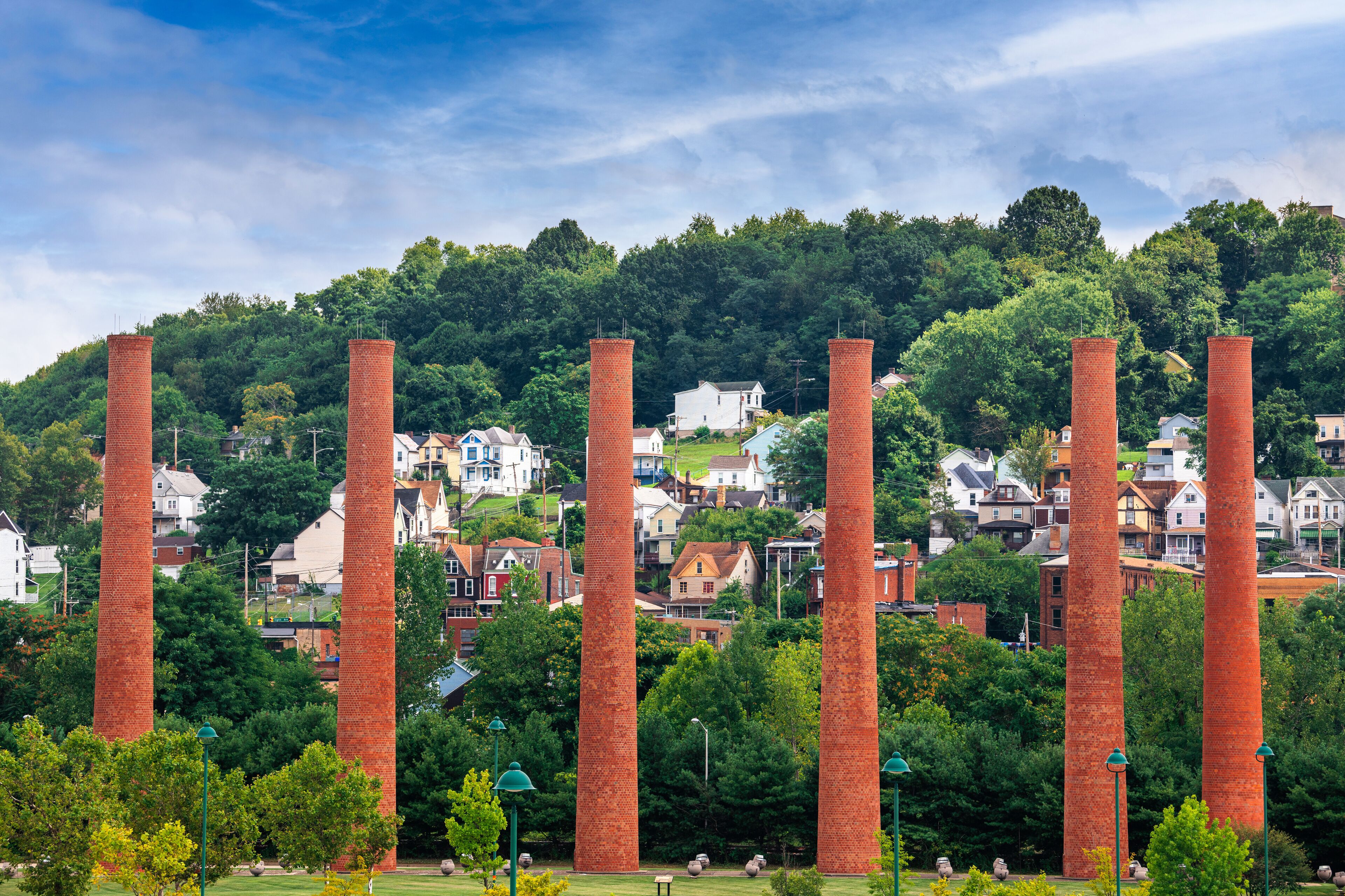 A park with tall brick chimneys, surrounded by trees and houses.