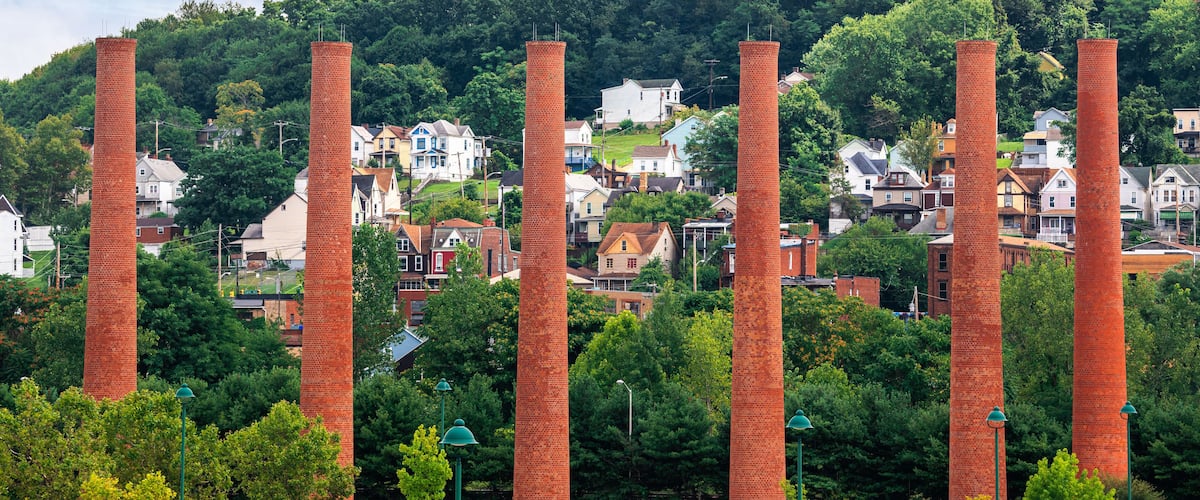 A park with tall brick chimneys, surrounded by trees and houses.