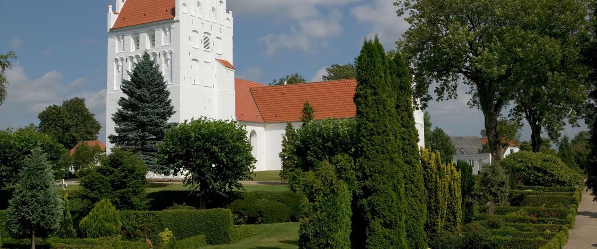 A white church with a red roof, surrounded by well-maintained gardens and trees.