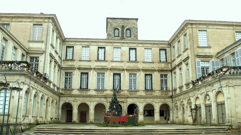 A historic building with a central courtyard, arched doorways, and a Christmas tree with a sleigh.