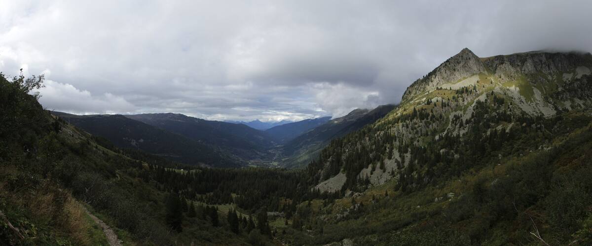 A mountainous landscape with a valley, a rocky peak, and a cloudy sky.