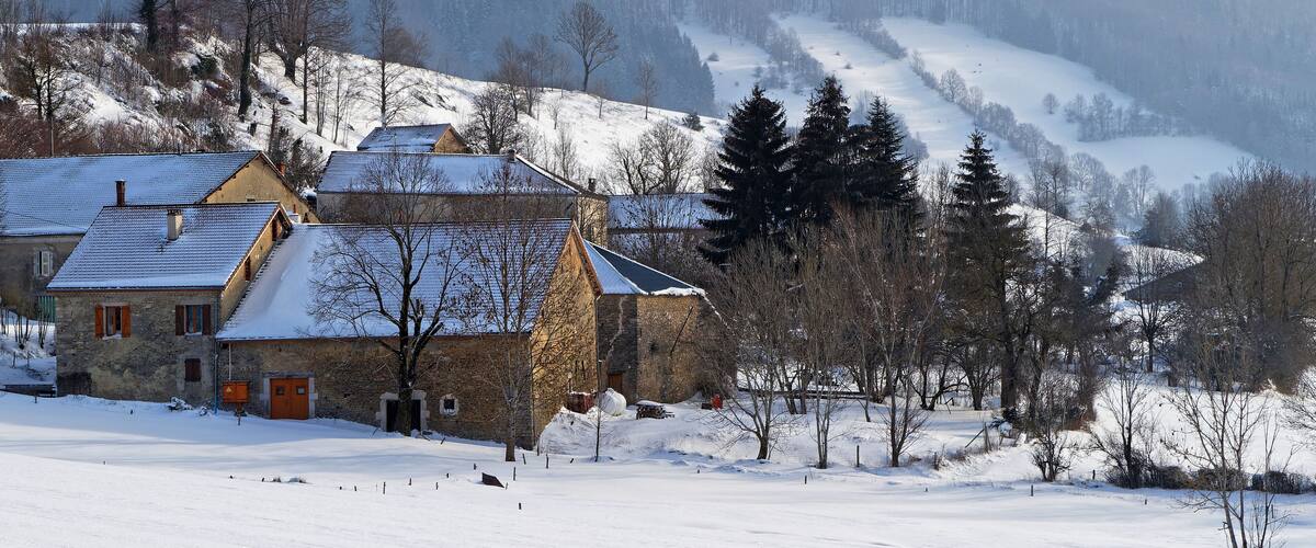 A snow-covered village with stone houses and a forested mountain in the background.