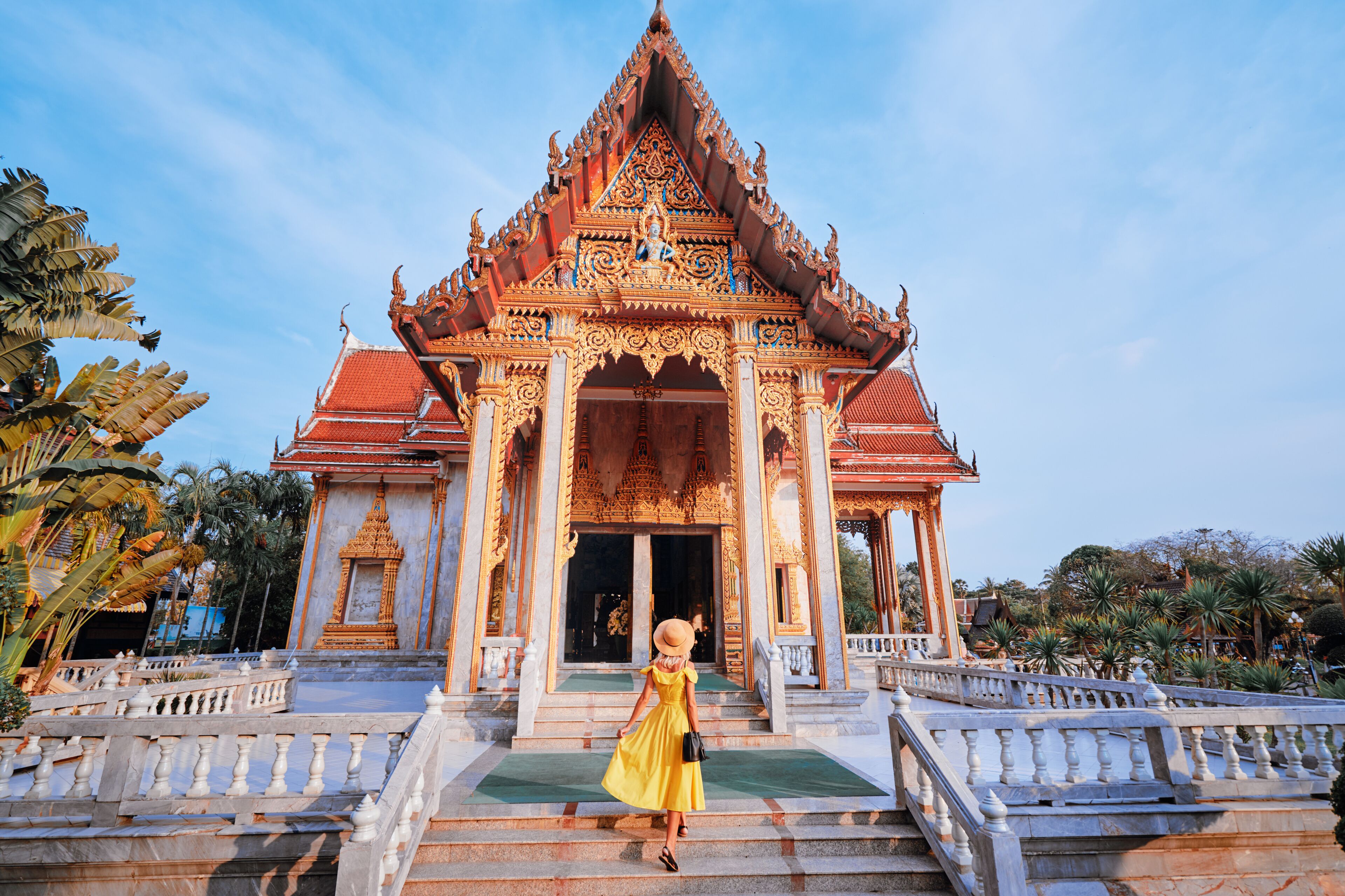 Travel by Asia . Young woman in hat and yellow dress walking near the Chalong buddhist temple on Phuket Island in Thailand.