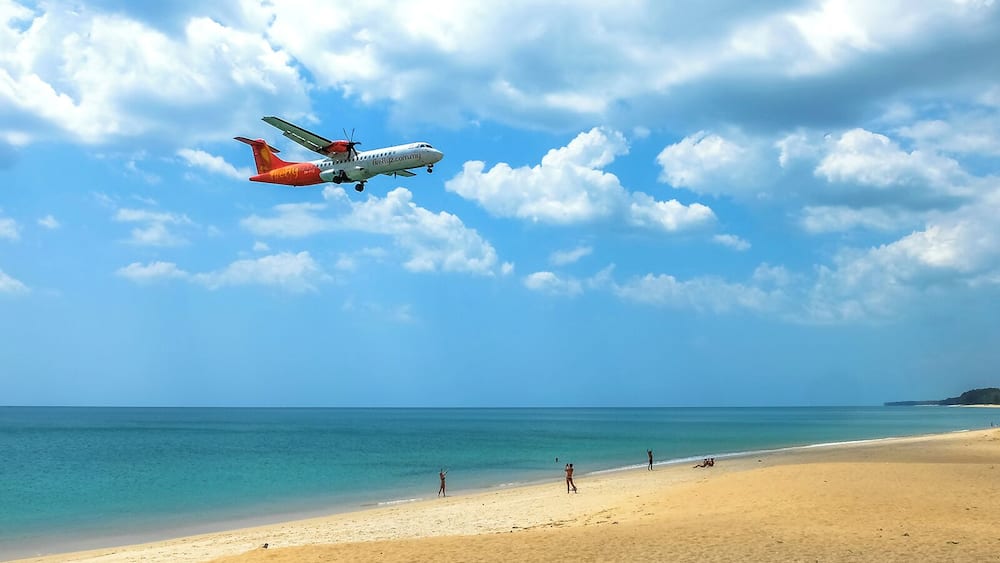 A beach with a plane flying overhead.