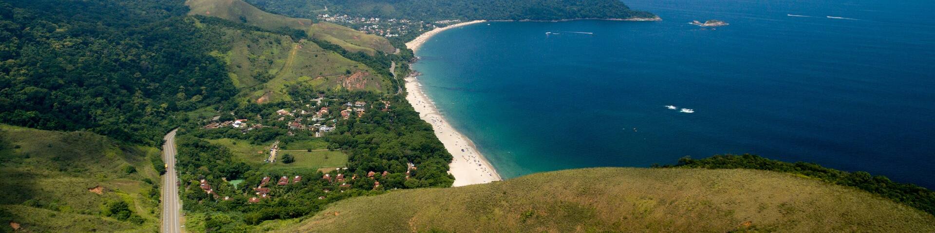 A coastal landscape with a winding road, a beach, and a mountainous backdrop.