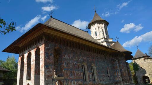 Una iglesia histórica con un campanario, frescos detallados y un cielo azul despejado.