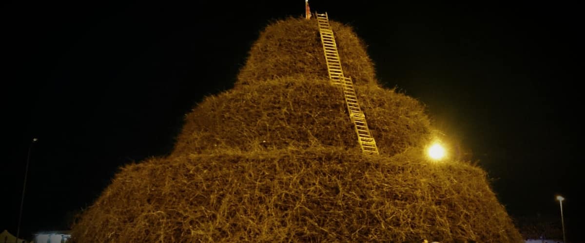A large haystack with a ladder leading to the top, surrounded by people.