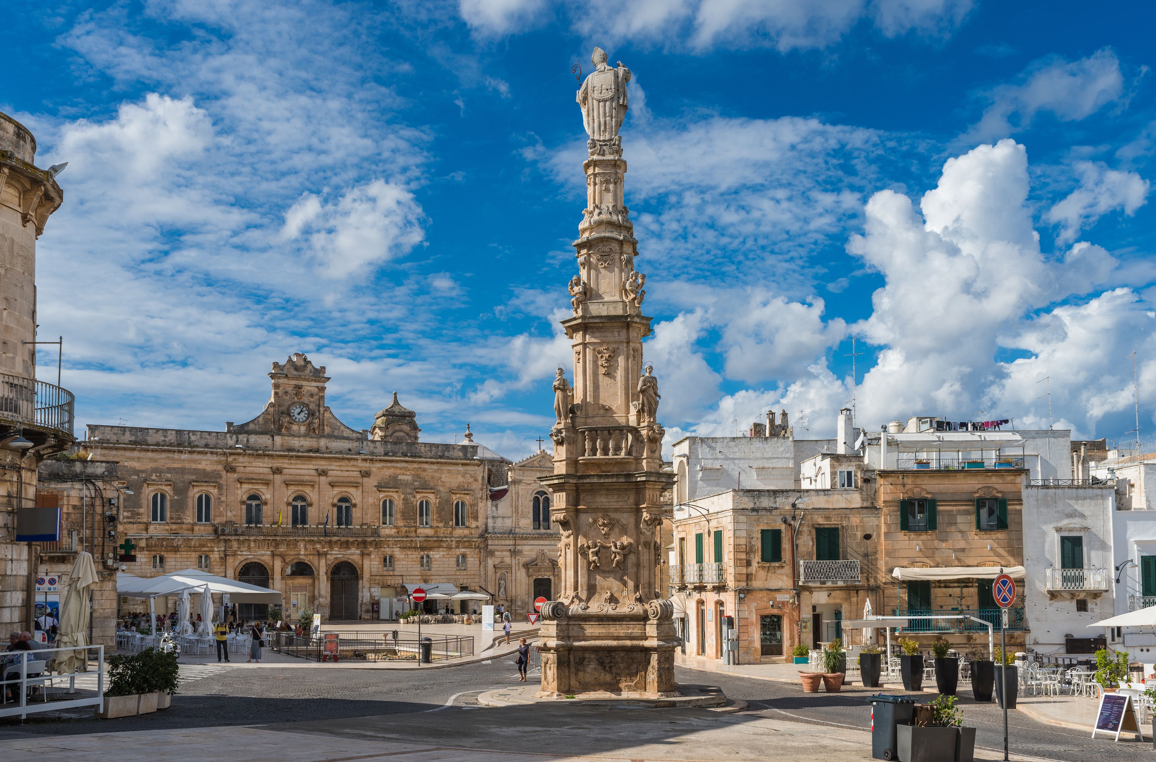 A historic square with a prominent monument, surrounded by classical architecture and cafes.