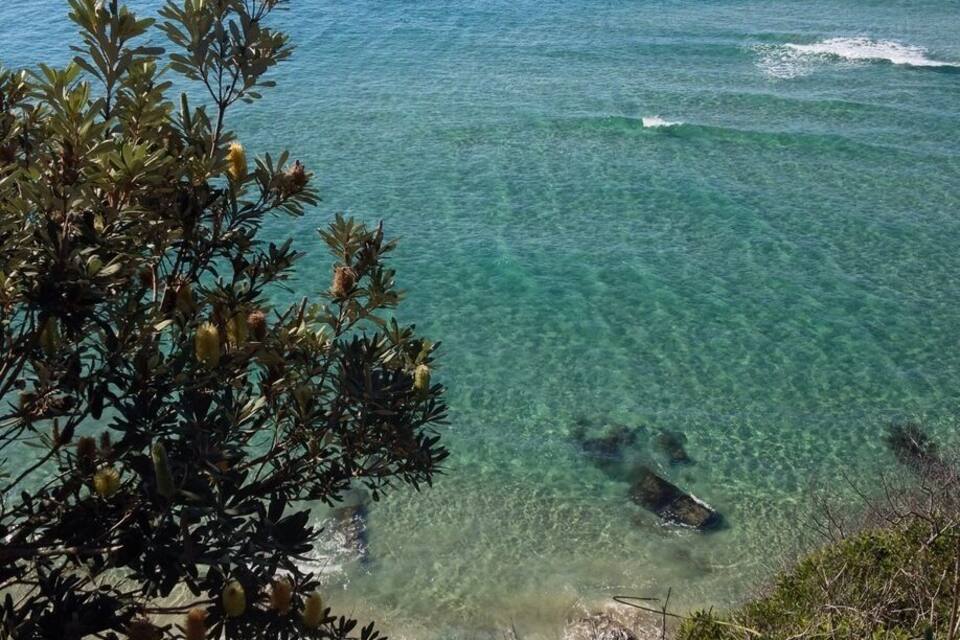 A coastal landscape with clear turquoise waters, a sandy beach, and lush greenery.