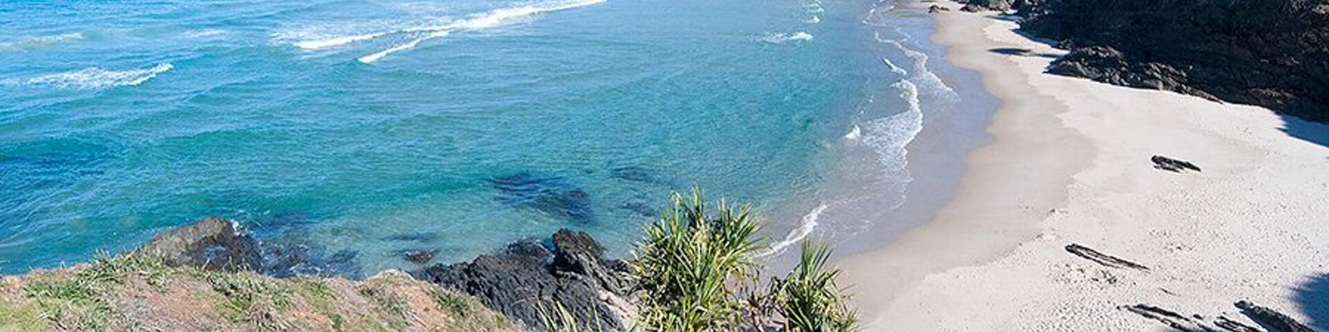 Un paisaje costero con una playa arenosa, aguas azules cristalinas y colinas verdes.