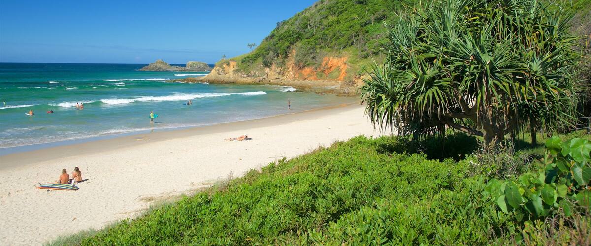 A beach with clear turquoise waters, a sandy shore, and lush greenery on the hillside.