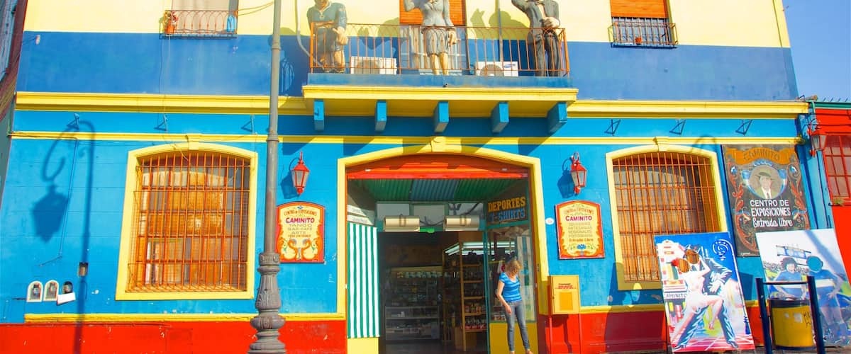 Un bâtiment aux couleurs vives, avec une façade bleue et jaune, un balcon orné de statues et une devanture de magasin affichant divers panneaux.
