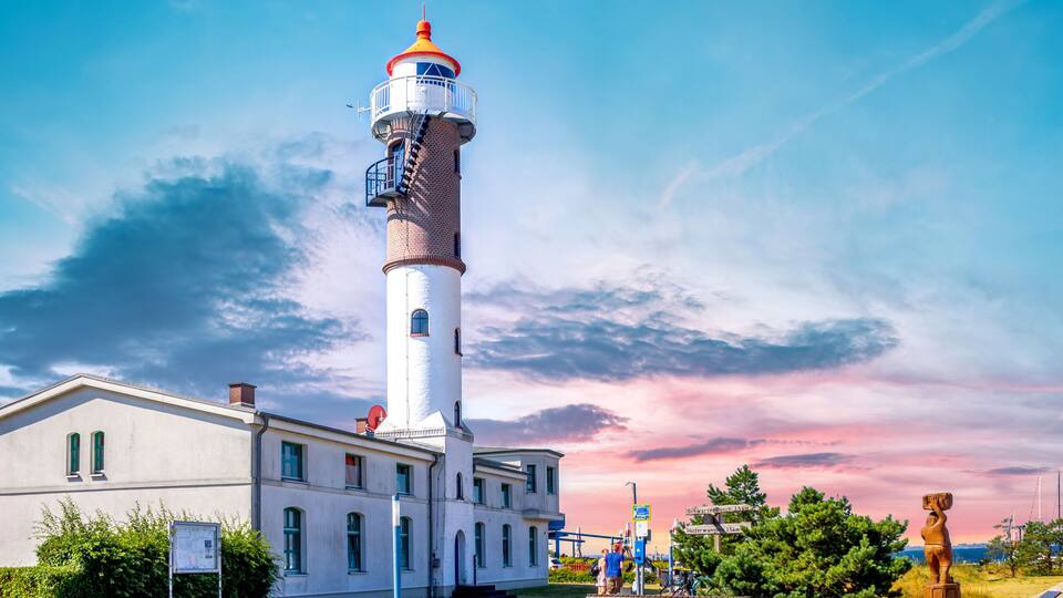 A lighthouse with a white building beside it, a clear sky, and a statue in the foreground.