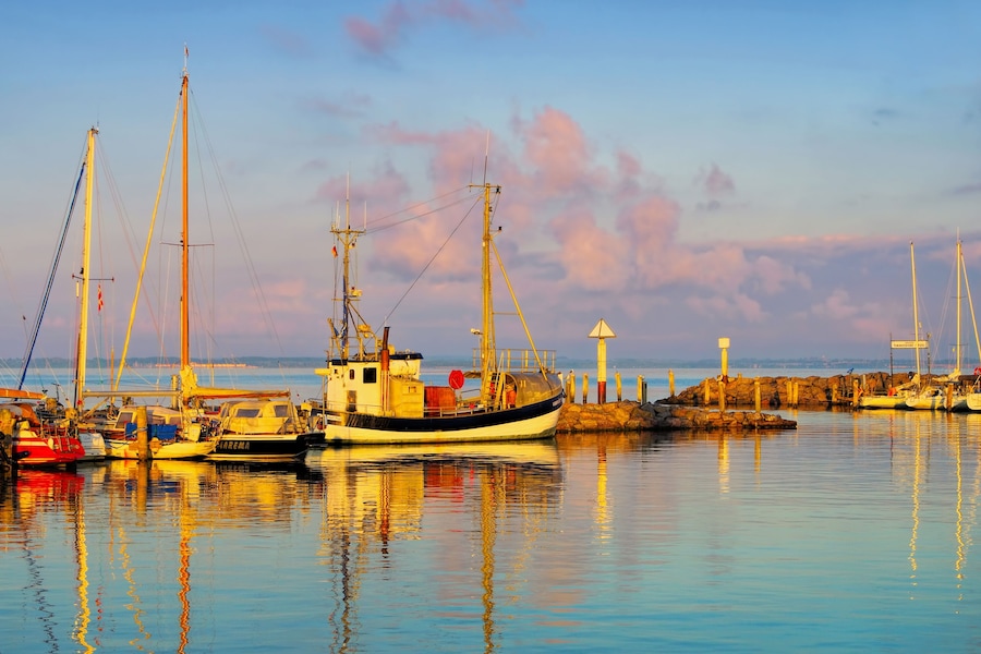 Un puerto con barcos, un faro y aguas tranquilas que reflejan el cielo.
