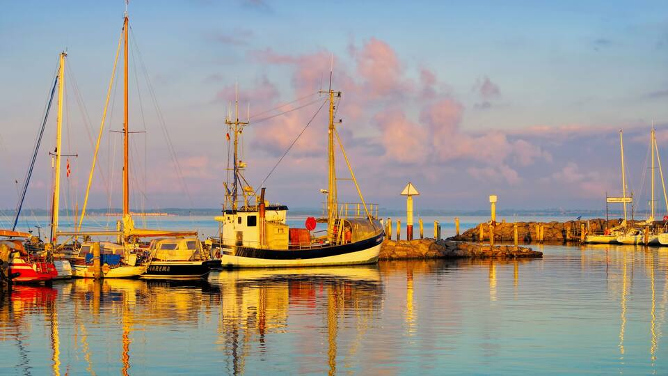 A harbor with boats, a lighthouse, and calm waters reflecting the sky.