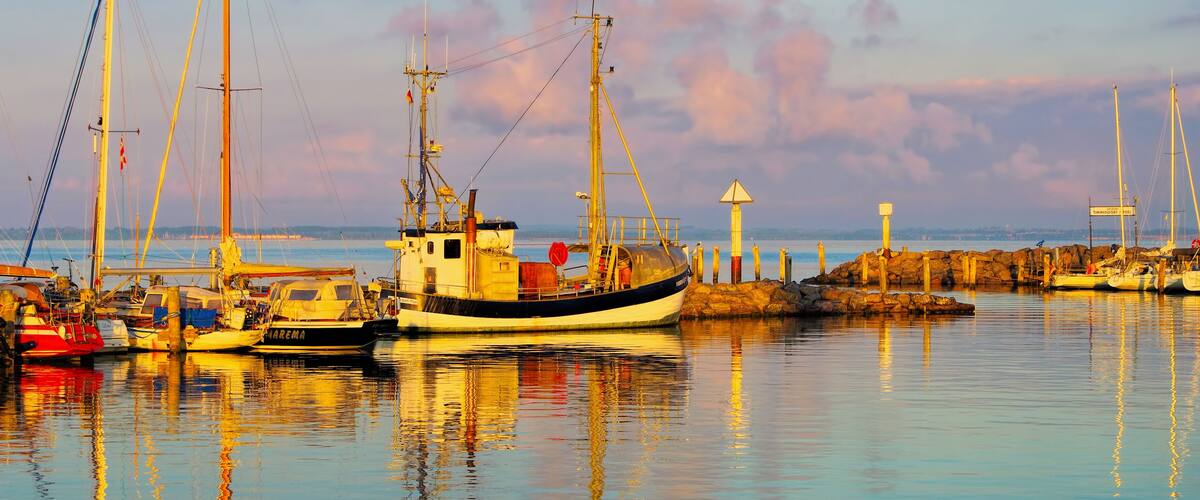A harbor with boats, a lighthouse, and calm waters reflecting the sky.