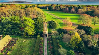 Un campo da golf con una torre, circondato da alberi e una vista sul mare in lontananza.