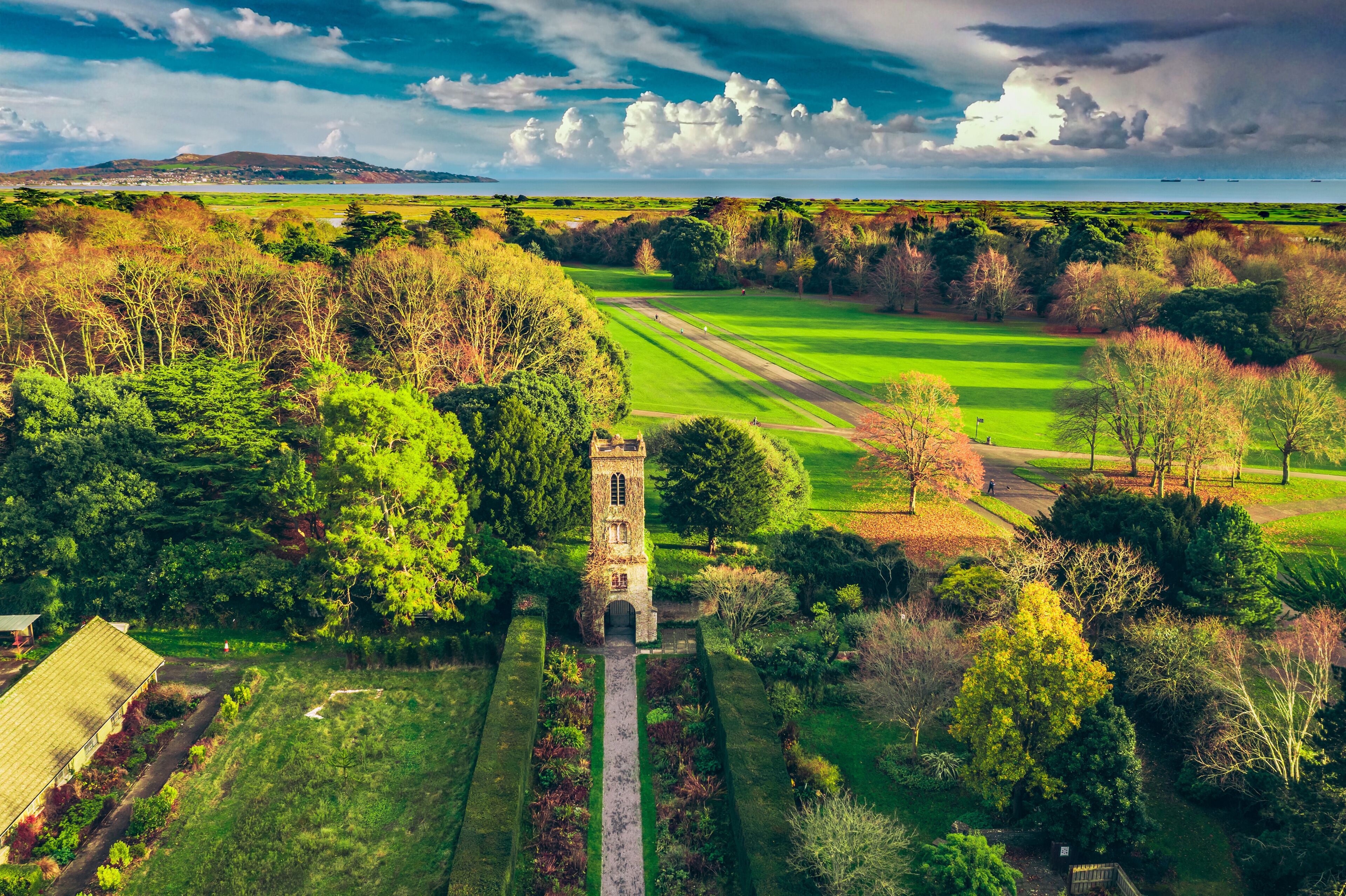 A golf course with a tower, surrounded by trees and a distant view of the sea.