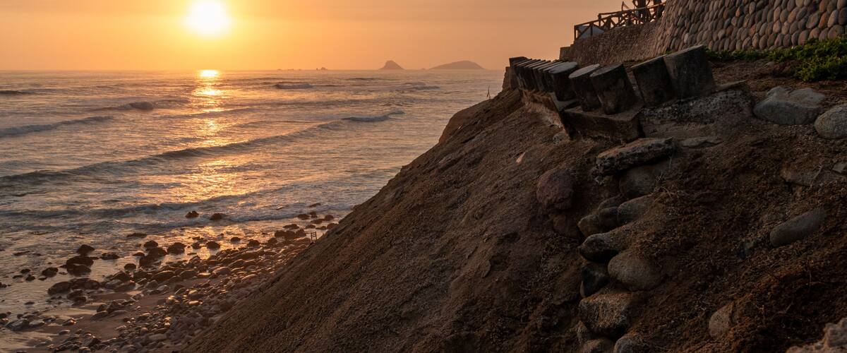 A sunset over a rocky beach with waves and a stone wall.