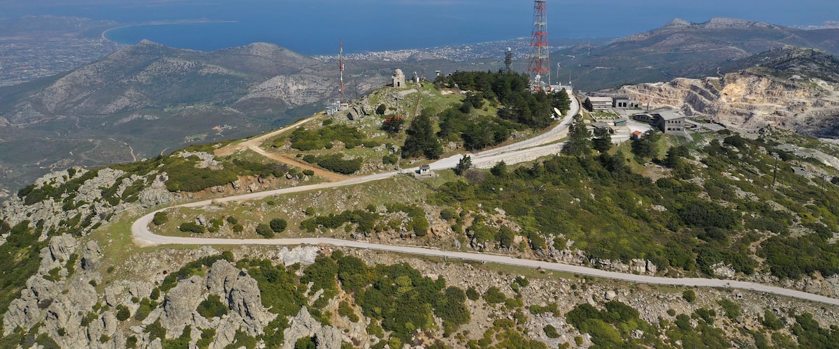 A mountainous landscape with a winding road, a small building, and a tall communication tower.