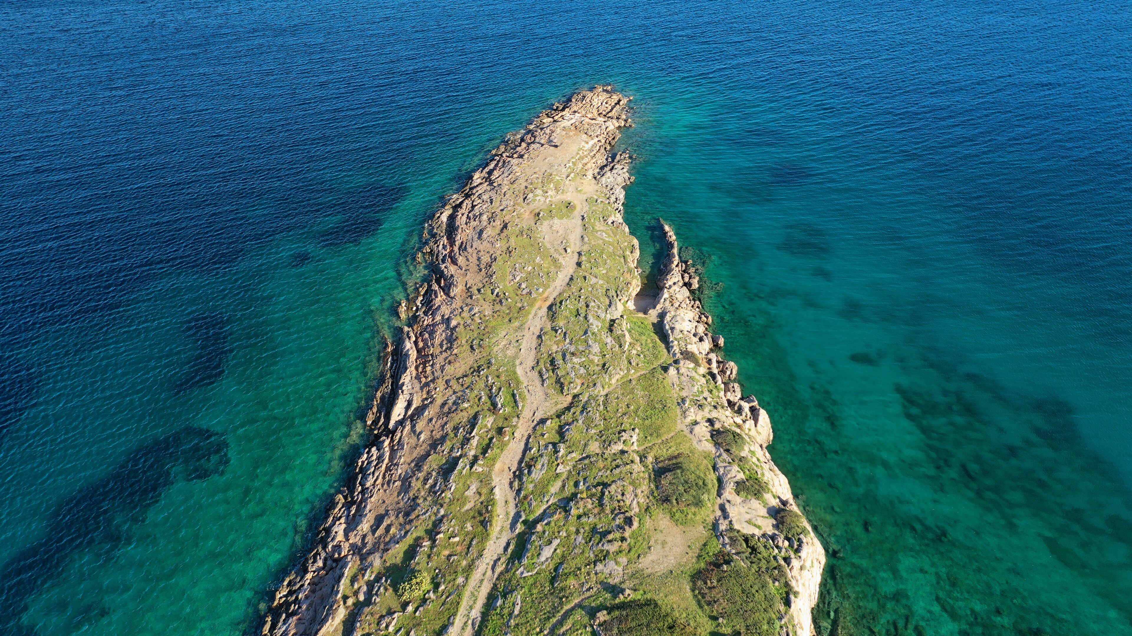 An aerial view of a rugged coastline with clear blue waters and rocky terrain.
