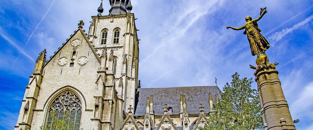 A historic cathedral with a tall spire, intricate window designs, and a statue on a column.