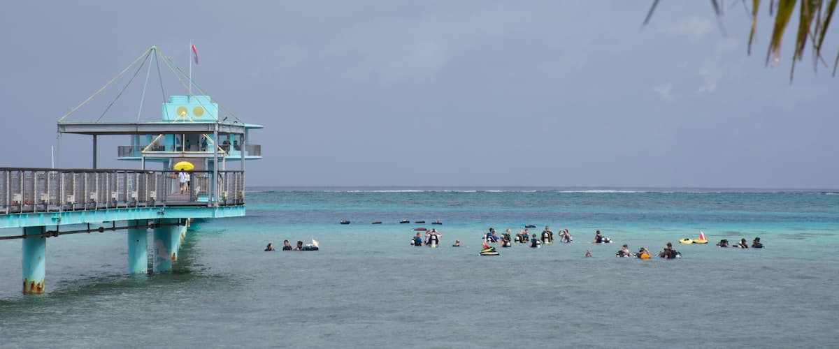 A pier extending into turquoise waters with people swimming and floating.