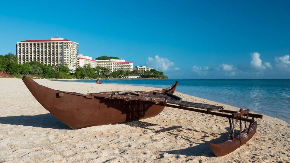 A boat on a sandy beach with a hotel in the background.