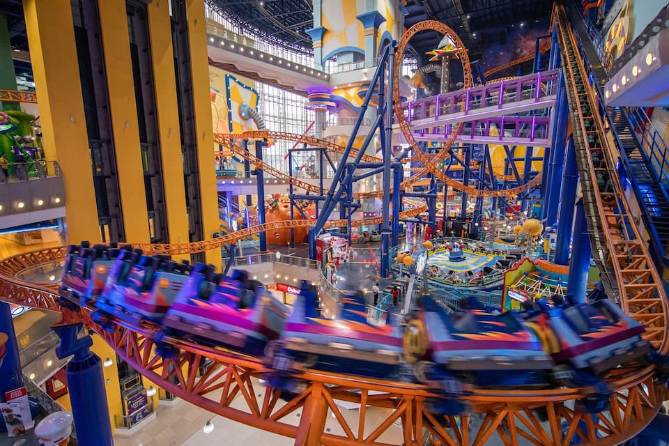 A large indoor amusement park with a roller coaster, Ferris wheel, and various rides.