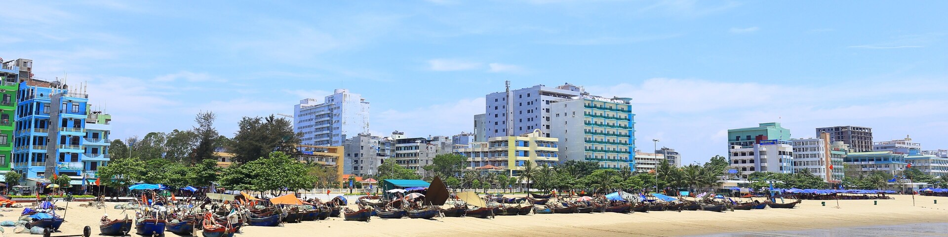 Una playa con barcos, una orilla arenosa y edificios de varios pisos al fondo.