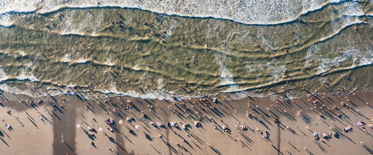 An aerial view of a beach with waves, people, and umbrellas.