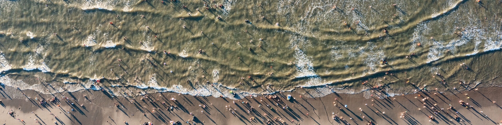 An aerial view of a beach with waves, people, and umbrellas.
