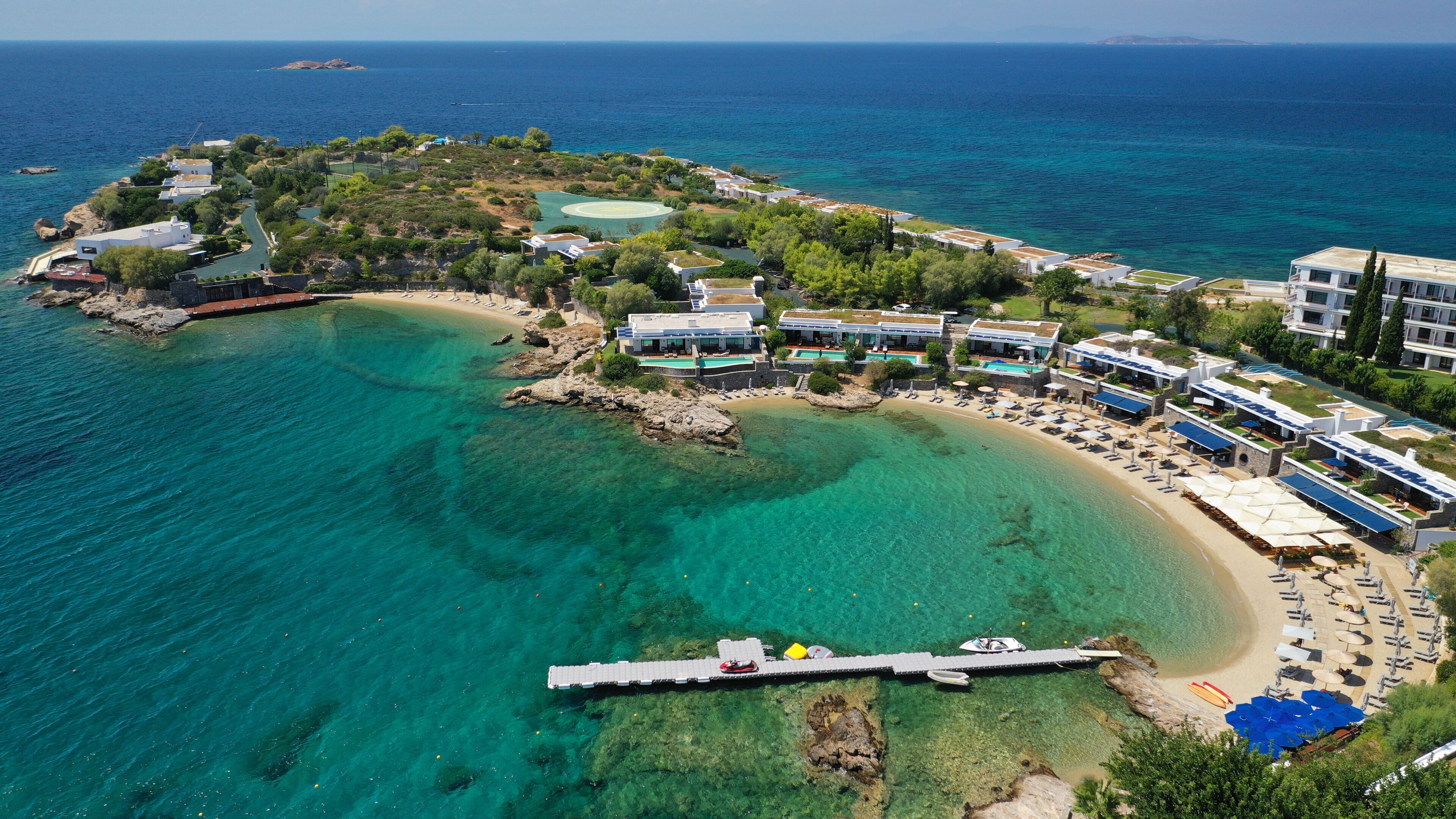 A coastal resort with clear turquoise waters, a sandy beach, and modern buildings with green roofs.