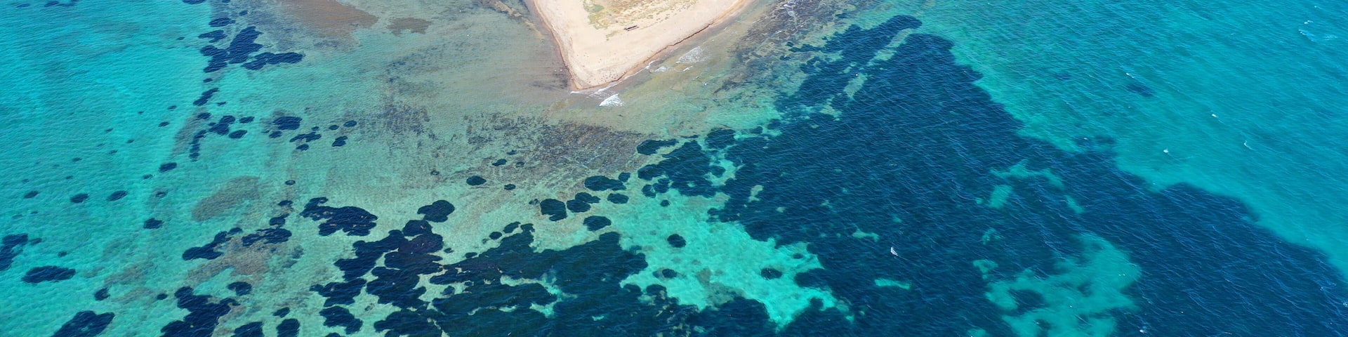 An aerial view of a coastal island with clear blue waters, sandy beaches, and scattered vegetation.