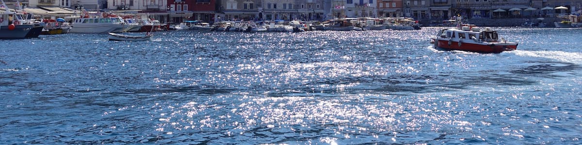 A coastal town with buildings on a hillside, boats on the water, and a clear sky.