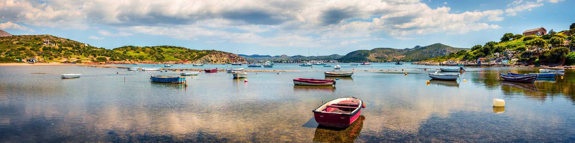 A calm bay with numerous boats anchored, surrounded by green hills and a clear blue sky.