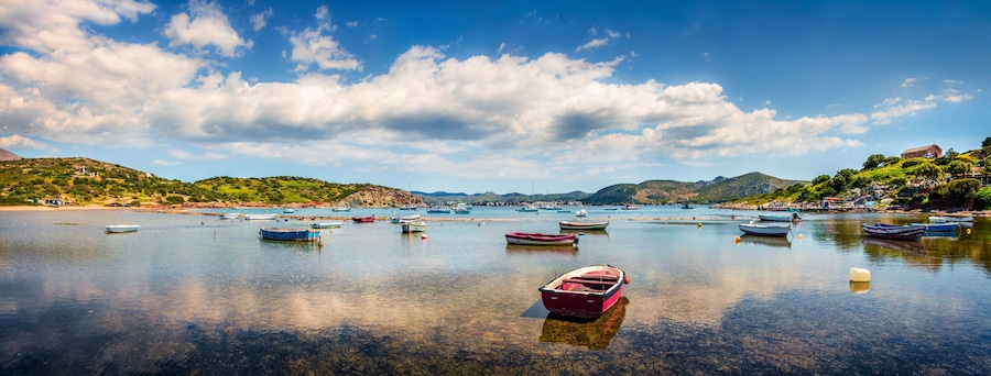 Una bahía tranquila con numerosas embarcaciones fondeadas, rodeada de colinas verdes y un cielo azul despejado.